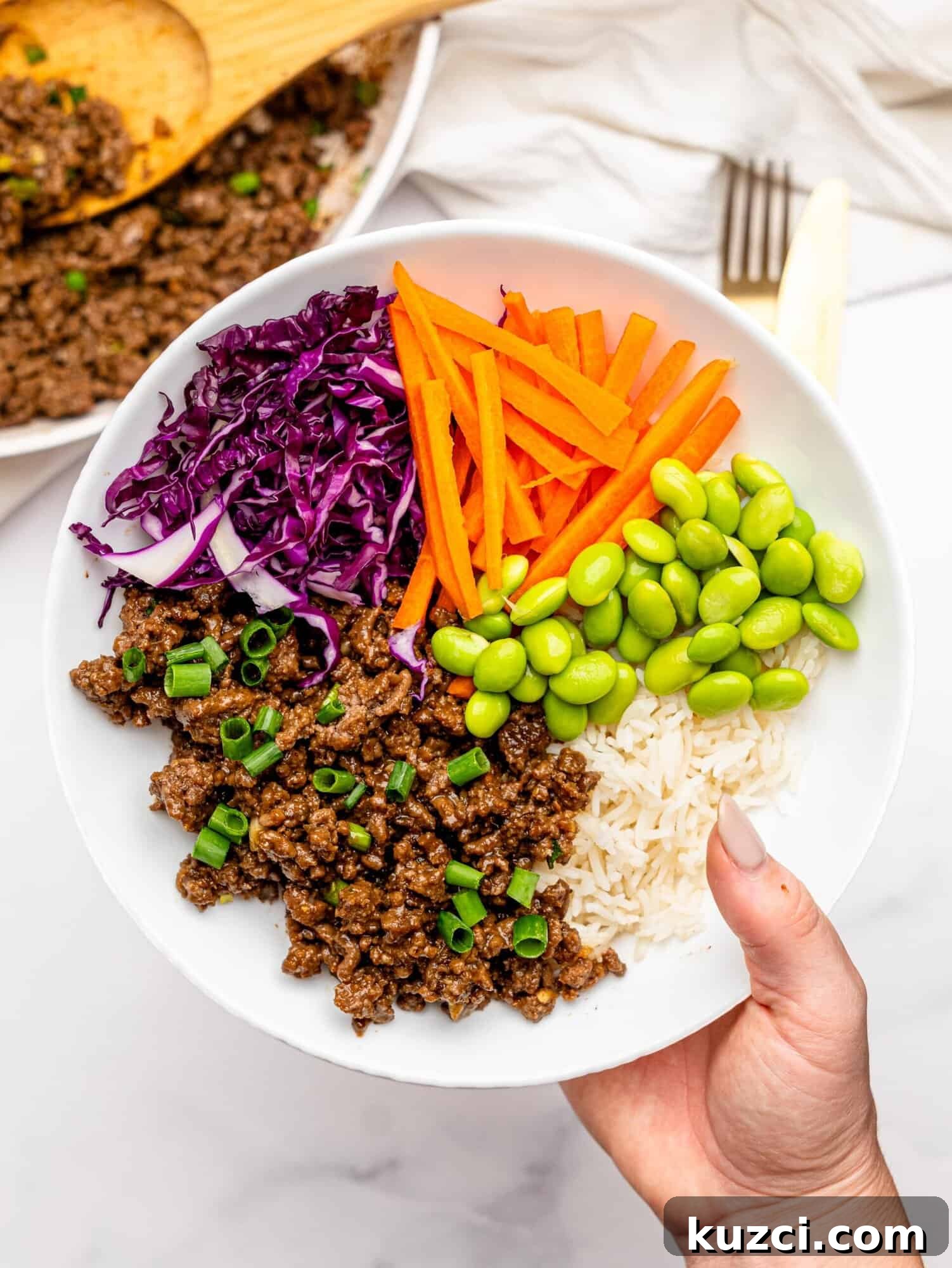 High Protein Teriyaki Beef Bowls for Meal Prep 6 A hand holding a teriyaki beef bowl.